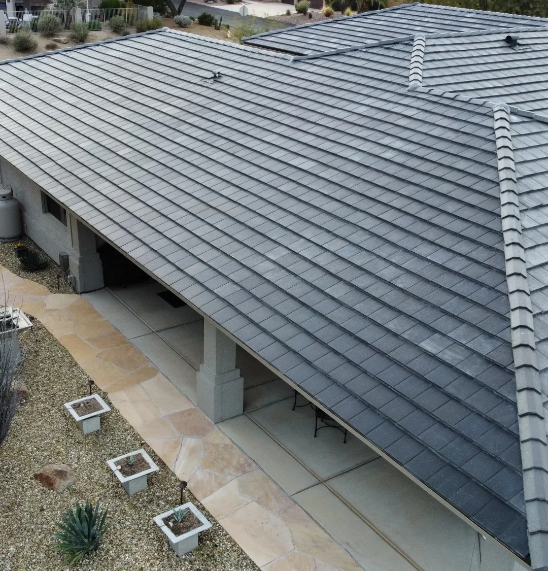 Aerial view of a house with a gray tiled roof, a covered patio, stone pathways, and landscaped yard with plants and mulch.